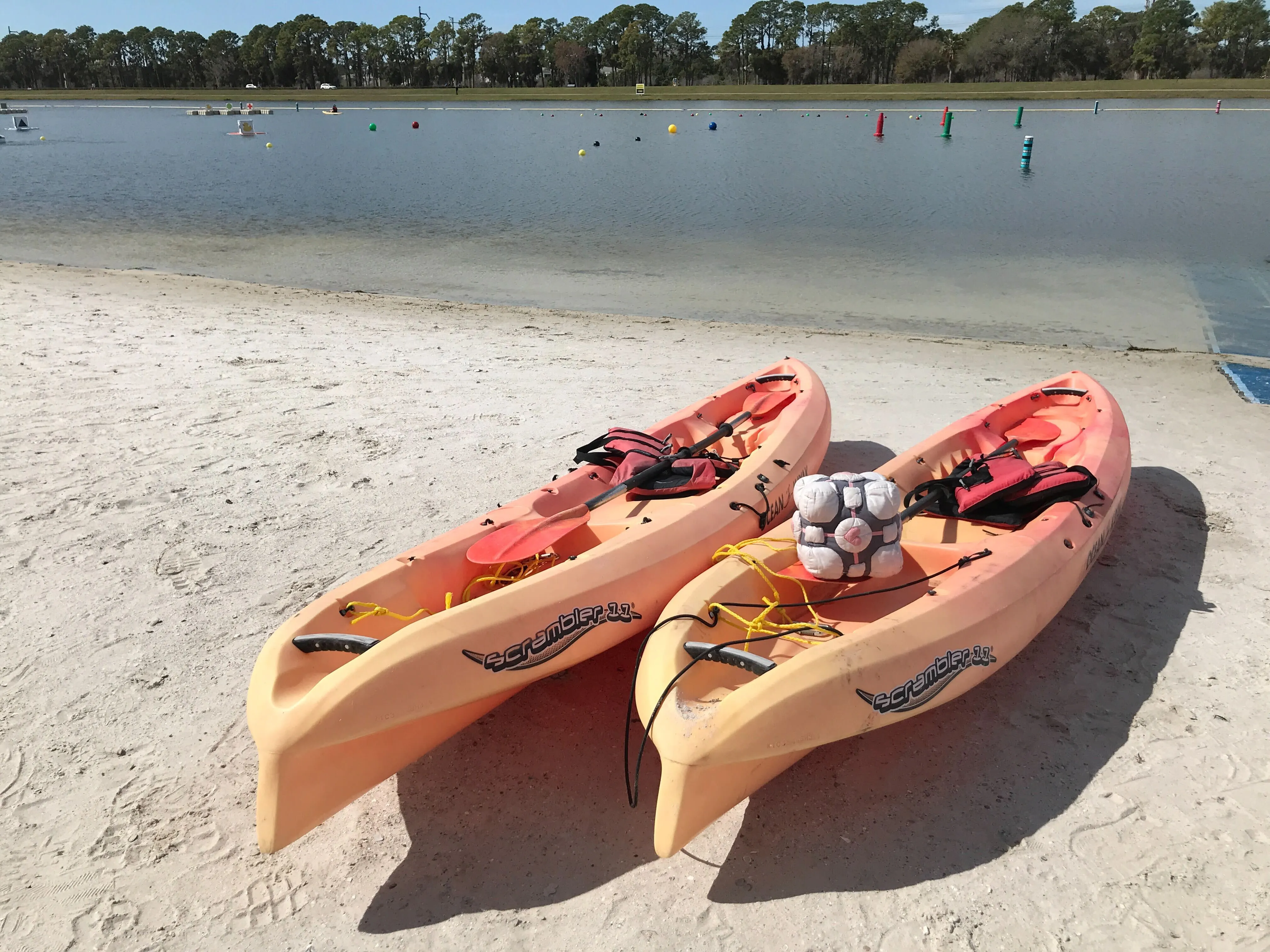 A hand-sewn companion cube sits on top of a yellow canoe next to a body of water.